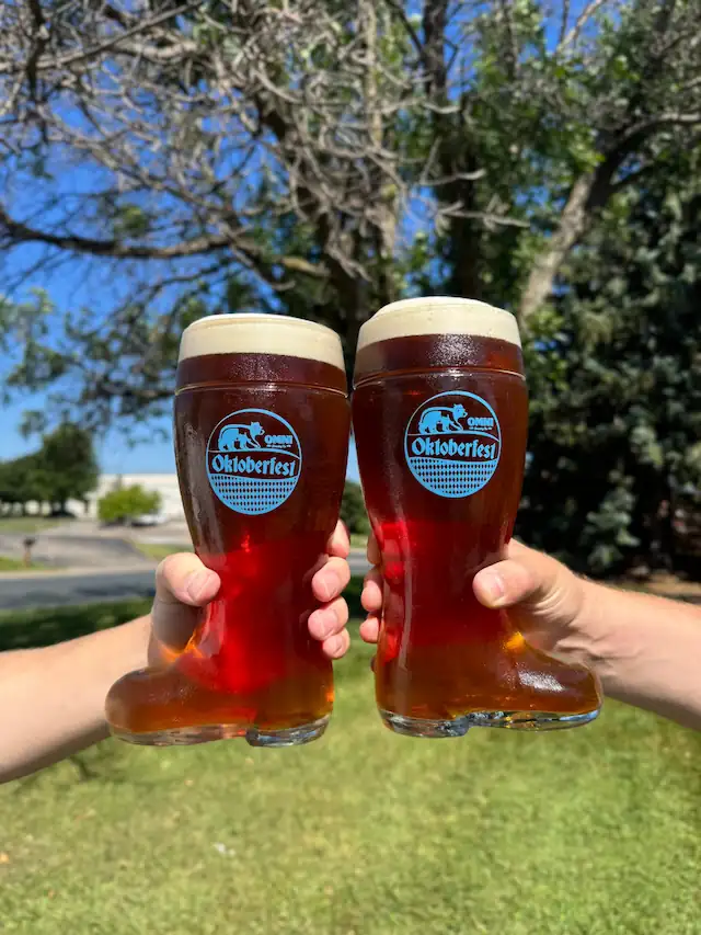 Two Oktoberfest glass boots being lifted on a sunny patio